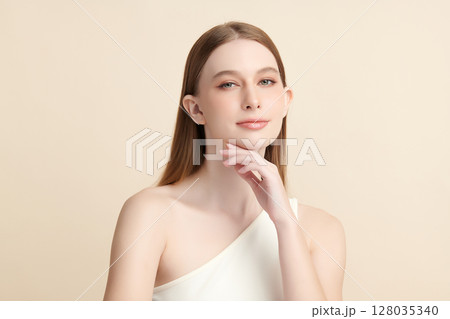 A beautiful young woman with clean, fresh skin against a beige background. Skincare, facial treatment, cosmetology, beauty, and spa. An elegant portrait of an woman. 128035340