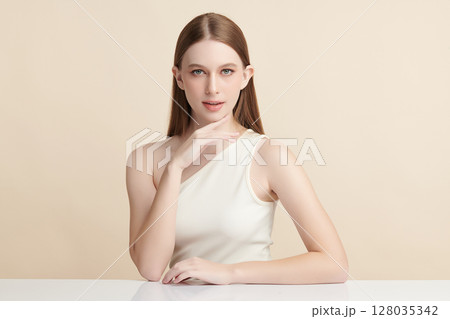 A beautiful young woman with clean, fresh skin against a beige background. Skincare, facial treatment, cosmetology, beauty, and spa. An elegant portrait of an woman. 128035342