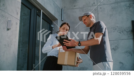 Businesswoman Receiving Her Package from Postal Service Worker, Signing POD on Tablet Computer 128039556