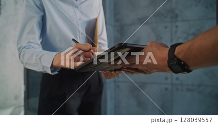 Close Up of Postman Delivering Small Parcel for Addressee, Getting Client's Signature on Digital Tablet Close Up of Postman Delivering Small Parcel for Addressee, Getting Client's Signature on Digital Tablet 128039557