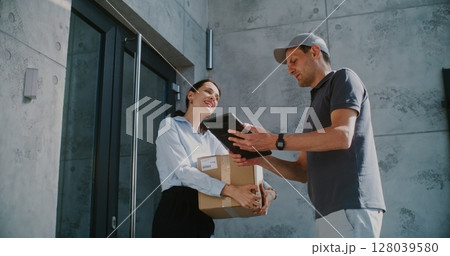 Businesswoman Receiving Her Package from Postal Service Worker, Signing POD on Tablet Computer 128039580