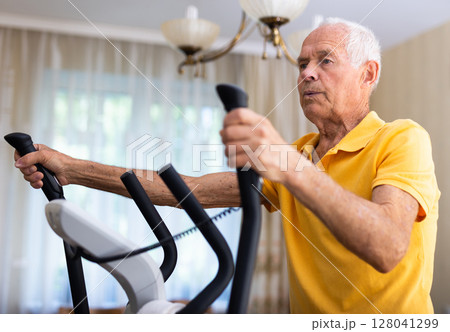 Senior man training on cross-trainer at home 128041299