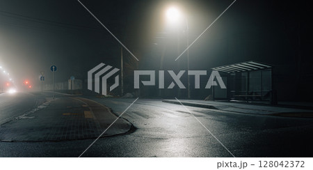 Urban night scene with a misty bus stop and glowing streetlights. 128042372
