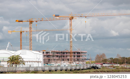Large construction site including several cranes working on a building complex, with cloudy sky timelapse 128045253