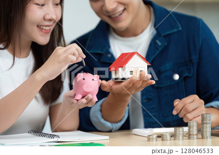 Couple Celebrating Financial Planning Success. Engaging with piggy bank and model house. 128046533