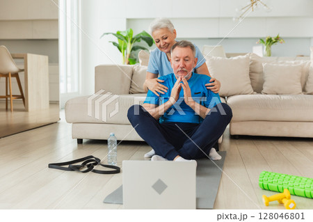 Yoga mindfulness meditation. Senior adult mature couple practicing yoga with online lessons in laptop. Old wife helping teaching husband meditating relaxing. Family doing breathing practice at home 128046801