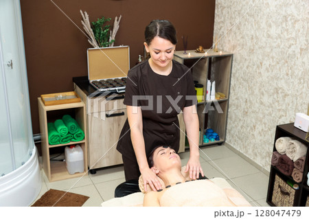 Female Massage Therapist Providing Relaxing Treatment to Patient on Couch in Beauty Salon Setting 128047479