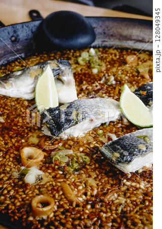 closeup of a sea bass paella with lime wedges 128049345