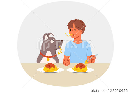 Little boy and dog eat spaghetti sitting at table, demonstrating friendship and trust 128050433
