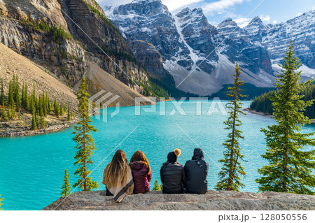 4人の女性旅行者がモレーン湖畔で眺める青い氷河湖と雪山。カナダ、アルバータ州 128050556