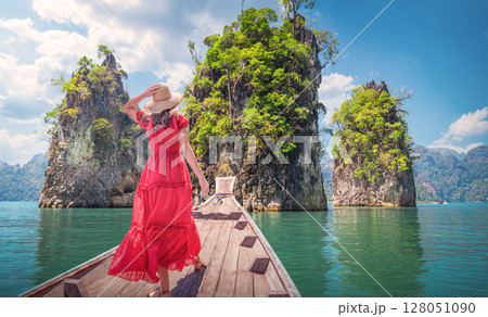 Panorama of the nature of famous places in Thailand - A woman in a Red dress looks at the landscape of mountains and rocks among the emerald waters of Cheo Lan Lake or sea in Khao Sok Park 128051090