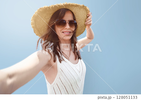 A female tourist traveler in a wide-brimmed hat takes a selfie on a blue monochrome background. Portrait of a Beautiful woman is a concept for travel advertising. A female tourist traveler in a wide-brimmed hat takes a selfie on a blue monochrome background. Portrait of a Beautiful woman is a concept for travel advertising. 128051133