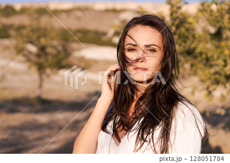 Woman with long hair is standing in a field Woman with long hair is standing in a field 128051784