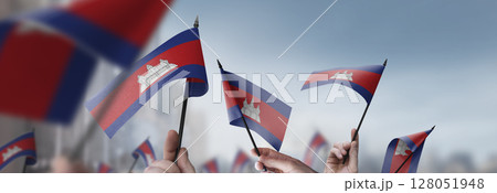 Cambodia flags in their hands on a blurred urban background Cambodia flags in their hands on a blurred urban background 128051948