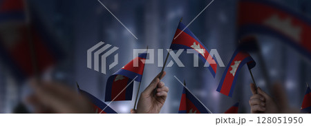 Cambodia flags in their hands on a blurred urban background Cambodia flags in their hands on a blurred urban background 128051950
