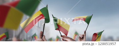 Benin flags in their hands on a blurred urban background Benin flags in their hands on a blurred urban background 128051957
