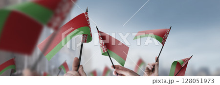 Belarus flags in their hands on a blurred urban background Belarus flags in their hands on a blurred urban background 128051973