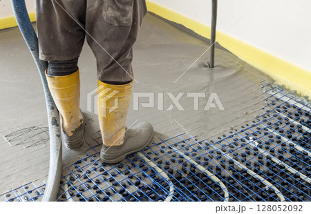 Man pouring concrete over floor heating installation in a new building. Modern construction system Man pouring concrete over floor heating installation in a new building. Modern construction system 128052092