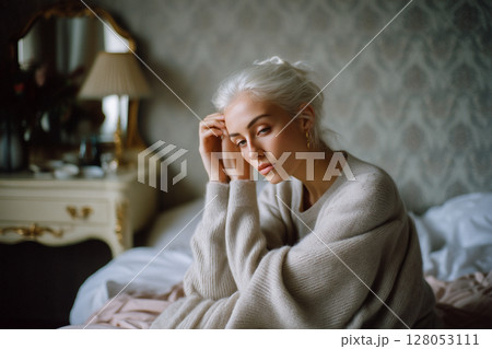 A woman is sitting on a bed with her head in her hands 128053111