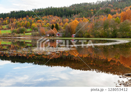 Lakeside scenery showcasing colorful autumn trees reflected on the calm water 128053412