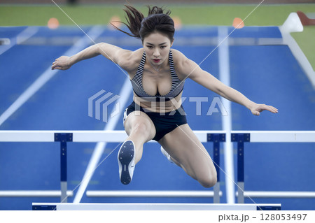 Woman is jumping over a hurdle 128053497