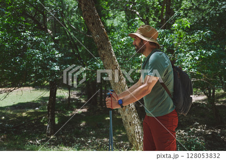 Bearded Male Hiker Exploring a Forest During a Summer Adventure with Trekking Poles and Backpack 128053832