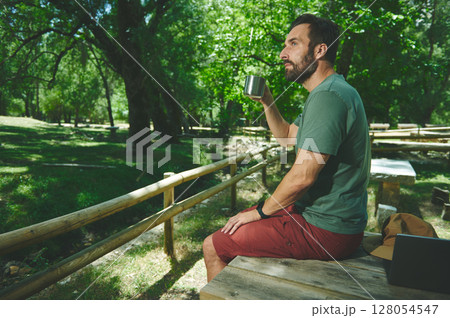 Bearded Man Enjoying Coffee in a Scenic Forest on a Serene Summer Day 128054547