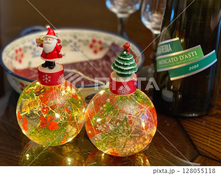 Glowing christmas ornaments with santa claus and a festive tree, reflecting on a wooden table Glowing christmas ornaments with santa claus and a festive tree, reflecting on a wooden table 128055118