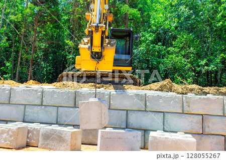 Construction vehicle uses crane to lift build retaining walls concrete blocks while working on concrete block wall Construction vehicle uses crane to lift build retaining walls concrete blocks while working on concrete block wall 128055267