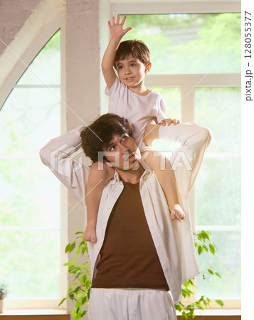 Everyday adventure. Father and son enjoying playful moment with child on dad's shoulders indoors 128055377