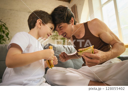 Father and son enjoying casual meal on relaxed Fathers Day celebration indoors Father and son enjoying casual meal on relaxed Fathers Day celebration indoors 128055402