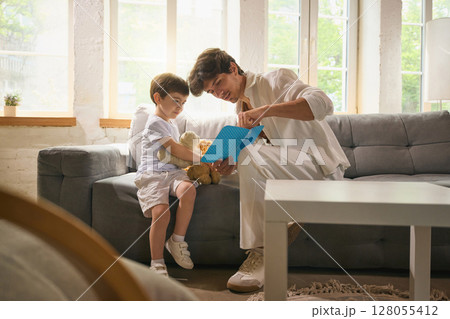 Father and son reading a handmade Fathers Day card together on the couch Father and son reading a handmade Fathers Day card together on the couch 128055412