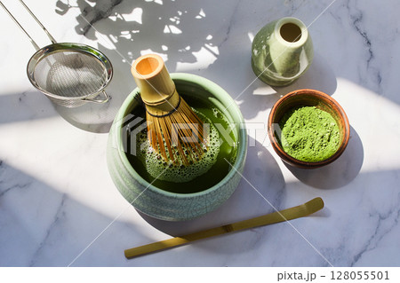 Traditional Matcha Preparation. Elegant matcha tea setup with a whisk, strainer, and green powder Traditional Matcha Preparation. Elegant matcha tea setup with a whisk, strainer, and green powder 128055501