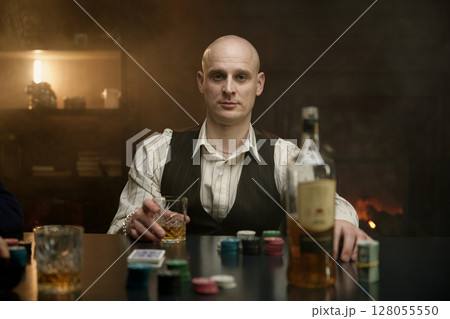 Man drinking whiskey at a poker table 128055550