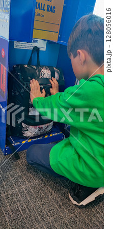 A young boy in a green sweatshirt is checking if a backpack fits into a Ryanair small cabin bag sizer at the airport. the travel preparation process, specifically budget airline luggage policies. A young boy in a green sweatshirt is checking if a backpack fits into a Ryanair small cabin bag sizer at the airport. the travel preparation process, specifically budget airline luggage policies. 128056016
