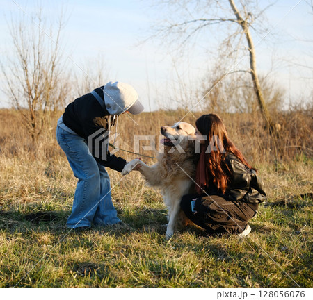 Girls Outdoors Asking Adorable Golden Retriever Dog To Give A Paw 128056076