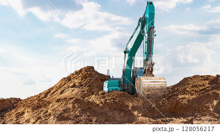 Excavator working on a construction site during daylight with a clear sky and soil pile Excavator working on a construction site during daylight with a clear sky and soil pile 128056217