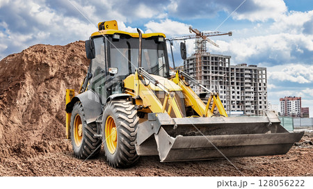 Excavator working on construction site with building and clouds in the background 128056222