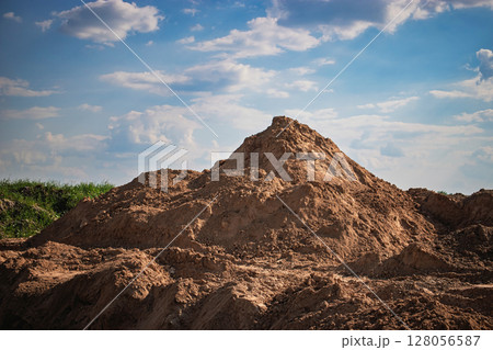 Construction site featuring a large mound of dirt under a blue sky with fluffy clouds in the afternoon 128056587