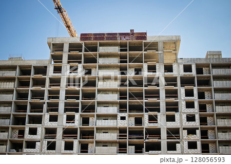 Building construction progresses on a high-rise structure in an urban area under bright blue sky 128056593