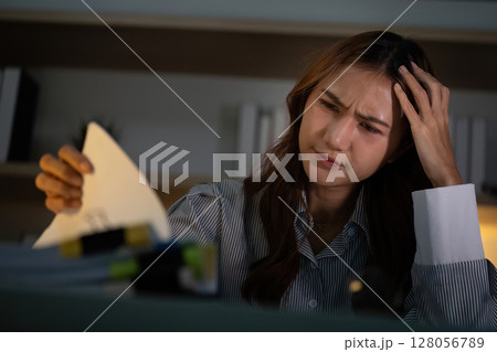 Late Night Work Stress. A woman struggling with paperwork and deadlines in a dimly lit office. 128056789