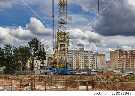 A large tower crane at a construction site against the backdrop of a modern monolithic house. Modern housing construction. industrial engineering. Construction of mortgage housing. 128056943