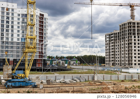 A large tower crane at a construction site against the backdrop of a modern monolithic house. Modern housing construction. industrial engineering. Construction of mortgage housing. 128056946