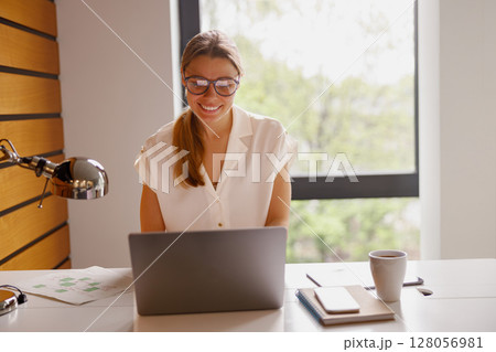 A Young Woman is Actively Working on Her Laptop in a Contemporary and Modern Workspace A Young Woman is Actively Working on Her Laptop in a Contemporary and Modern Workspace 128056981