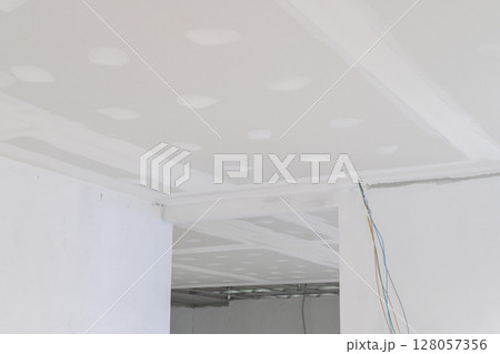 Gypsum board ceiling in building interior undergoing renovation. Smooth plastering on edges, with visible electrical wire, creates feeling of work in progress toward smooth finish 128057356