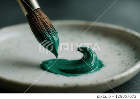 Detail of Artists Brush Laying Rich Emerald Pigment Curl on Ceramic Palette 128057672