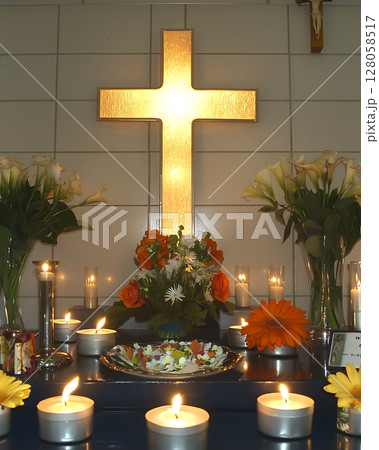 A lit candle is on a table in front of a cross 128058517