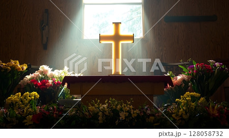 A cross is lit up in a church with flowers in the background 128058732
