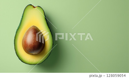 Half of ripe avocado with seed displayed on a smooth green background. Minimalistic composition highlighting natural texture and fresh healthy ingredient. 128059054