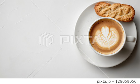 Cup of cappuccino with beautiful latte art served on a white plate with a biscuit over a textured white background. Minimalistic cozy coffee break. 128059056